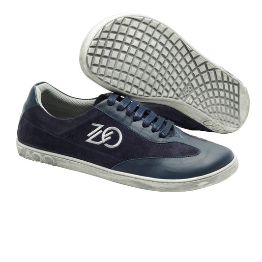 Wir präsentieren den Queensburry Marine von ZAQQ: ein Paar Barfuß-Sneaker in Dunkelblau mit weißer Sohle und Schnürsenkeln, gefertigt aus dunkelblauem Leder für verbesserten Komfort beim Laufen. Diese Schuhe verfügen über das ZAQQ-Logo an der Seite und ein strukturiertes Muster auf der sichtbaren Sohle, wodurch Stil und Komfort perfekt miteinander kombiniert werden.