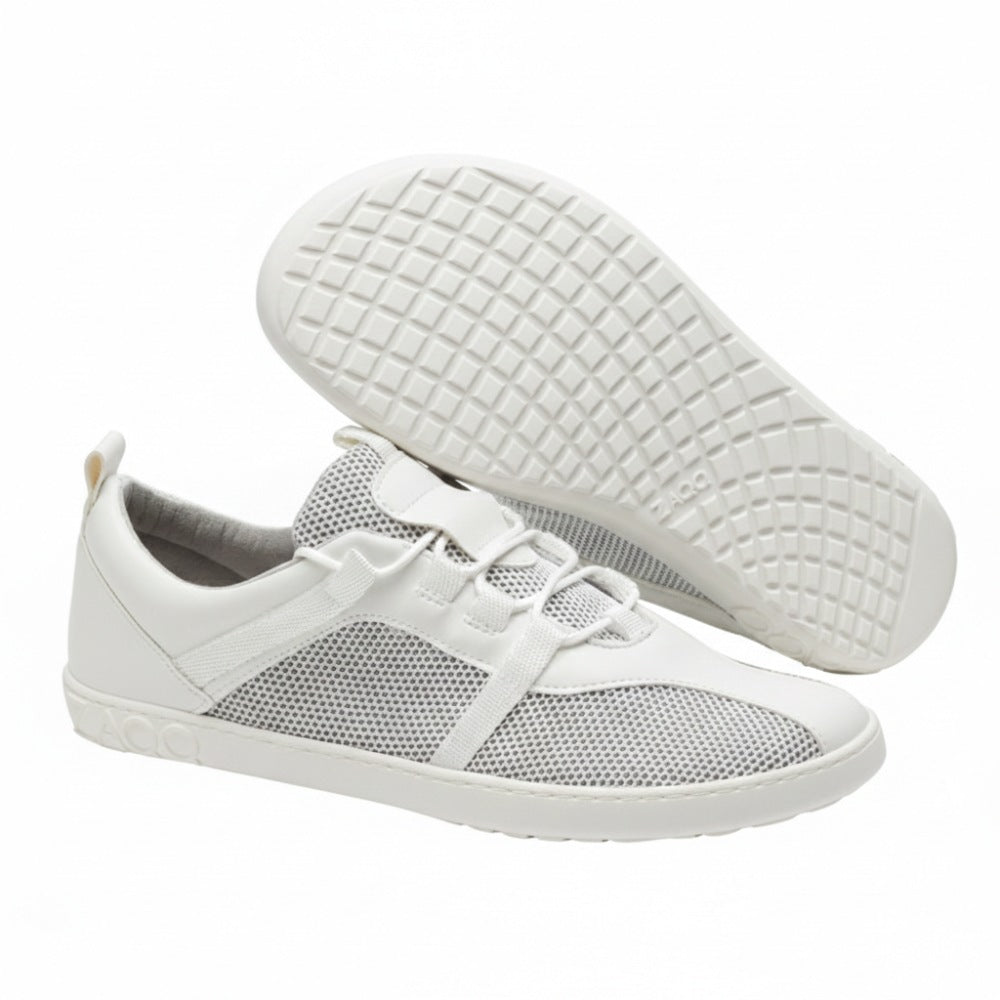 Die weißen MCQARTER-Sportschuhe von ZAQQ mit atmungsaktiven Mesh-Details und Gummisohlen werden ausgestellt. Ein Schuh steht aufrecht, während der andere angewinkelt ist, um das Profil zu zeigen. Dies unterstreicht ihre präzise Verarbeitung, die einen Komfort bietet, der dem eines Barfußschuhs ähnelt.
