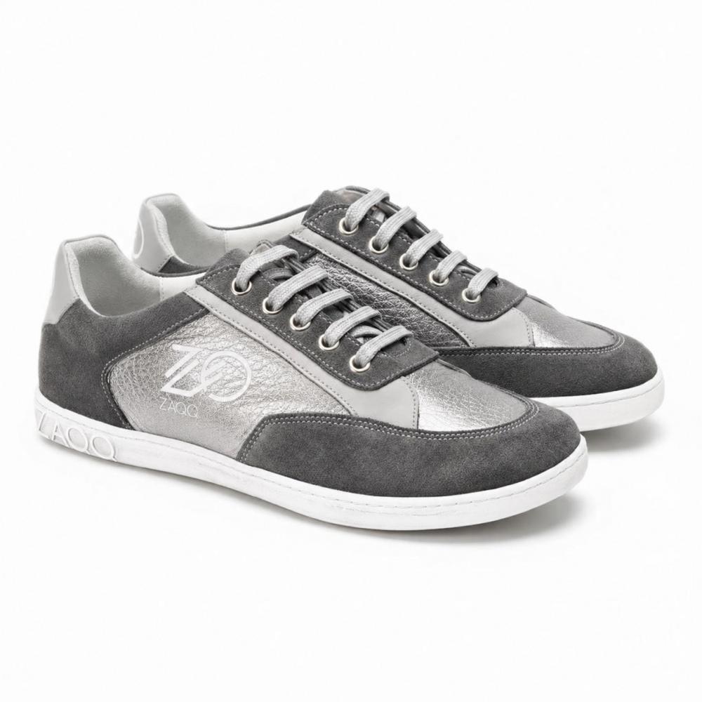Un paio di sneaker OQTAV Grey di ZAQQ, realizzate in morbida pelle scamosciata con inserti strutturati. Con lacci argentati e il caratteristico logo Zagoo sul lato e sul tallone, queste eleganti scarpe sono presentate fianco a fianco su uno sfondo bianco.