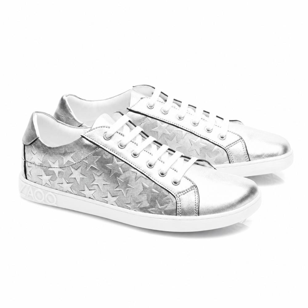 Le SLOQ Stars Silver-Sneaker di ZAQQ hanno lacci bianchi e motivi a stella sui lati, completati da una suola bianca con il logo VAOO sul tallone. Queste scarpe si distinguono per un design elegante e moderno con una finitura metallica lucida.